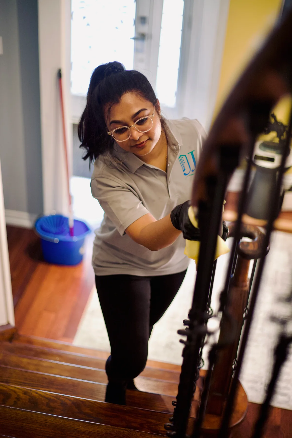 A uniformed J&J cleaner working on a wooden staircase inside a home